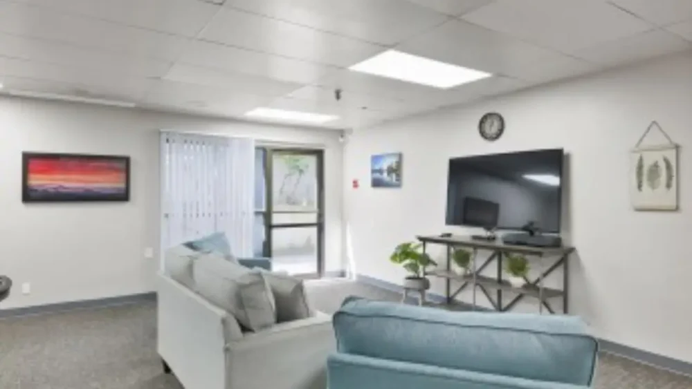 A living area with a light blue couch and armchair, a TV on a stand, and a picture on the wall